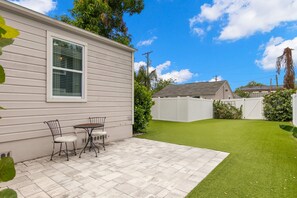 A patio with a table and chairs, a small lawn, and a white fence.