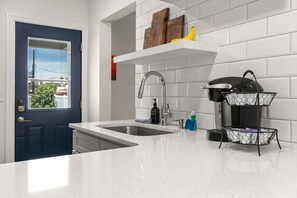 A kitchen with a double sink, white subway tiles, a blue door, and a metal rack with dishes.