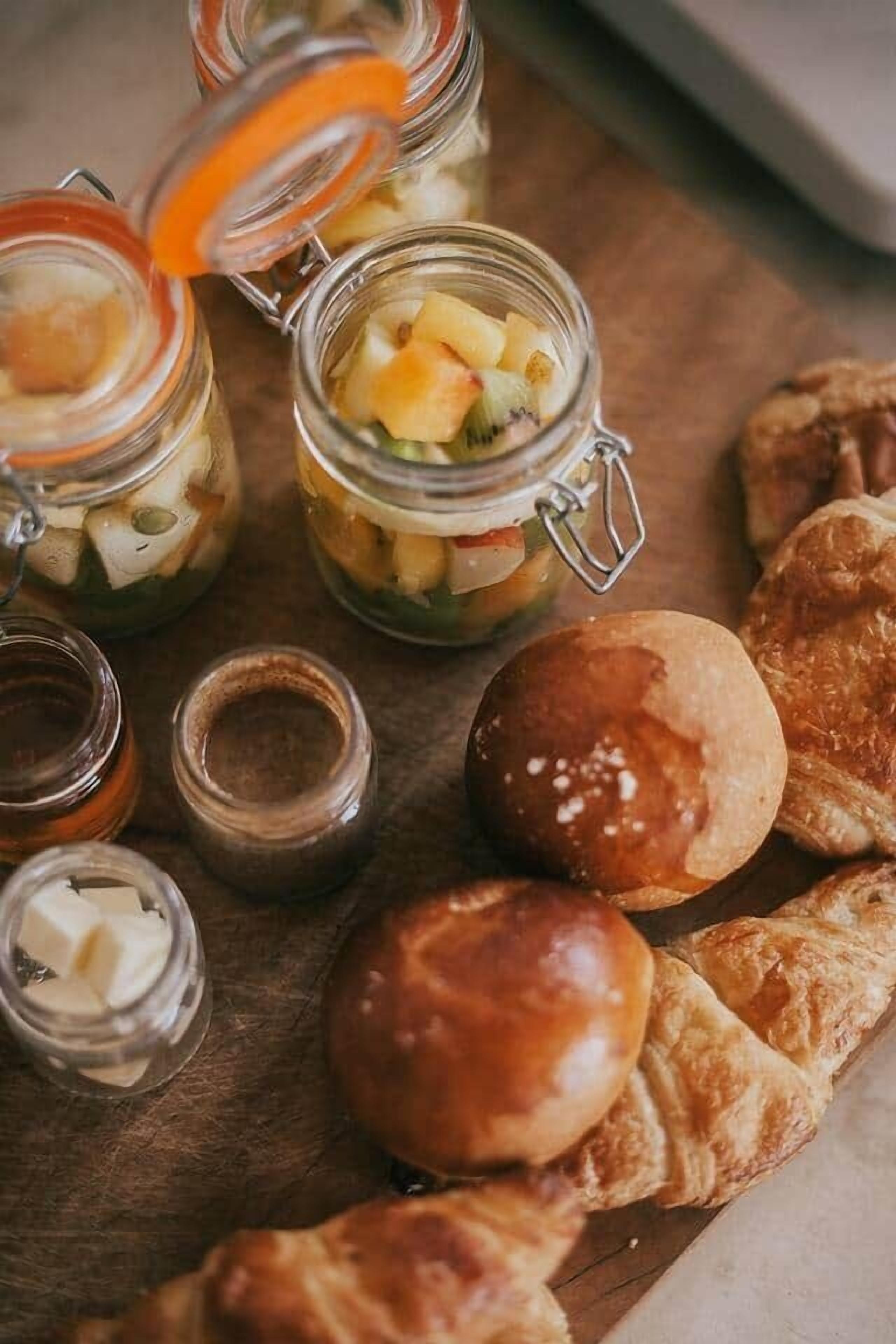 Een houten tafel met potten ingelegde vruchten, boter en gebak.