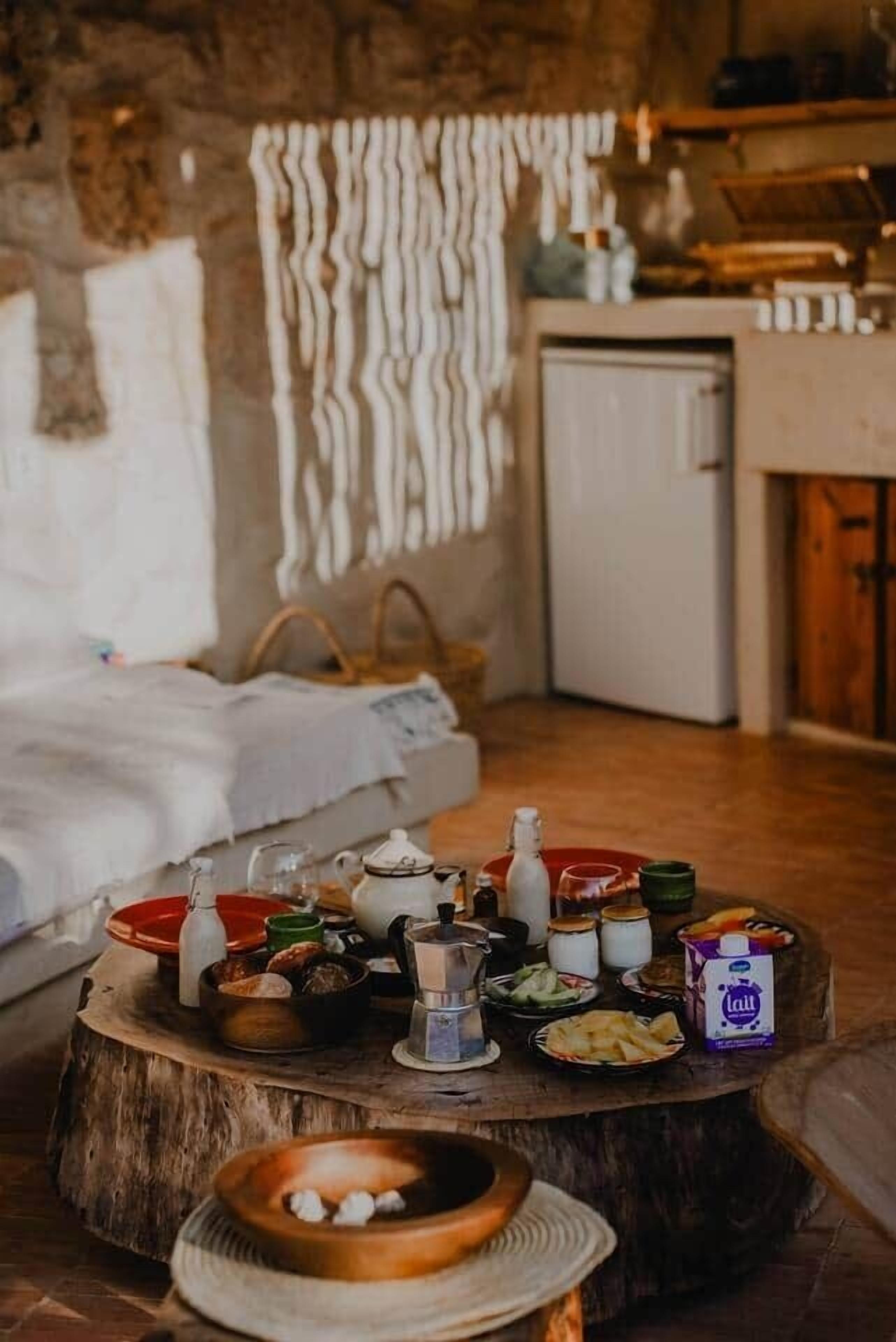 Une pièce chaleureuse avec une table en bois rustique, dressée avec divers aliments, et un petit réfrigérateur.