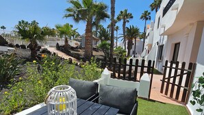 Eine Terrasse mit Tisch und Stühlen, umgeben von Palmen und einem weißen Zaun.
