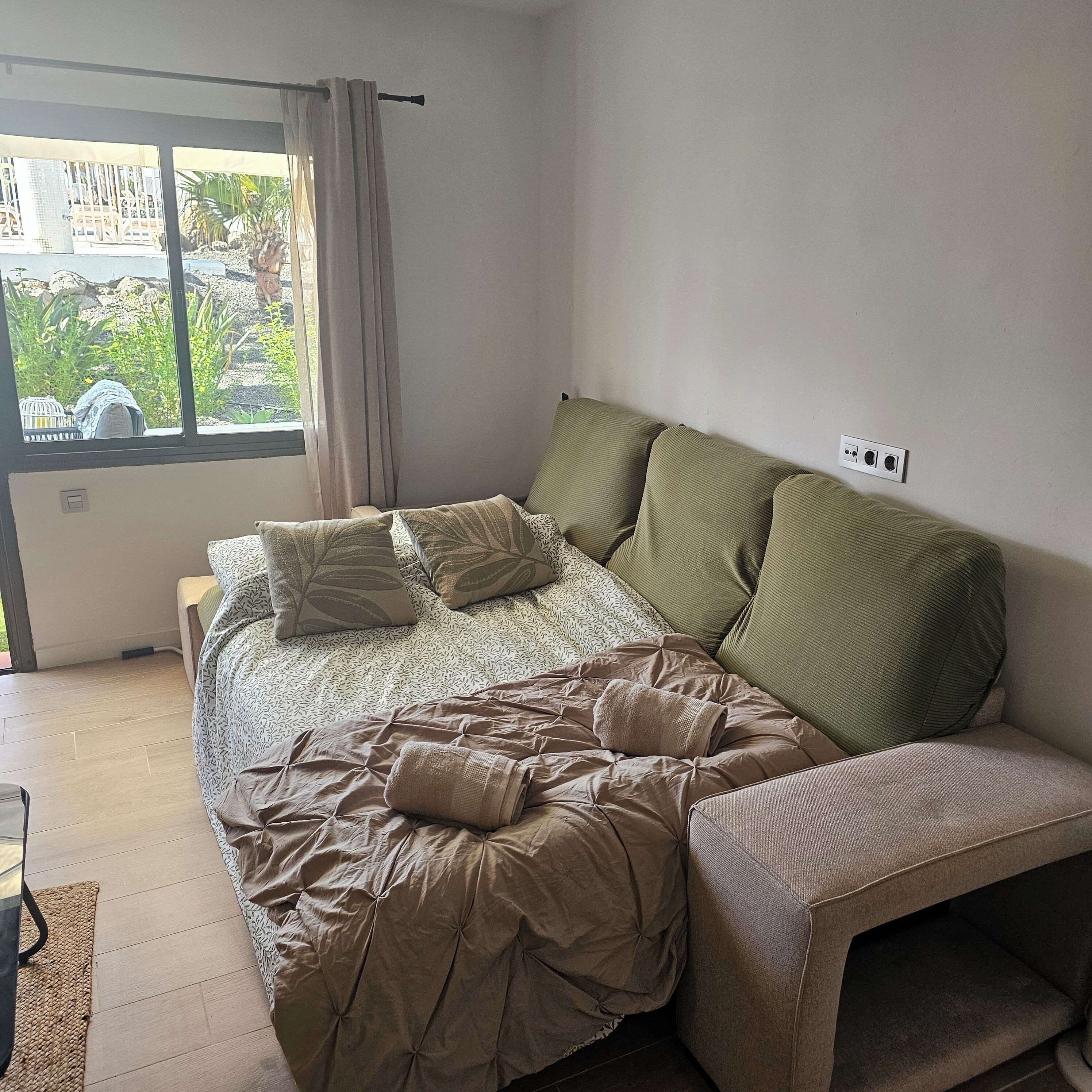 Quarto com cama, janela com cortinas, sofá e tomada na parede.