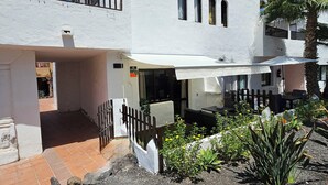 Ein weißes Gebäude mit Balkon, überdachter Außenbereich und kleinem Garten mit Pflanzen und Blumen.