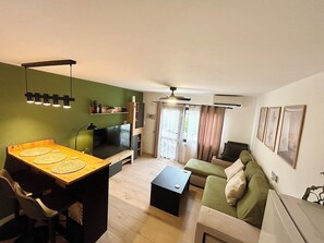 Un salon comprenant un téléviseur, un canapé, une table basse et un coin repas avec une table et des chaises.