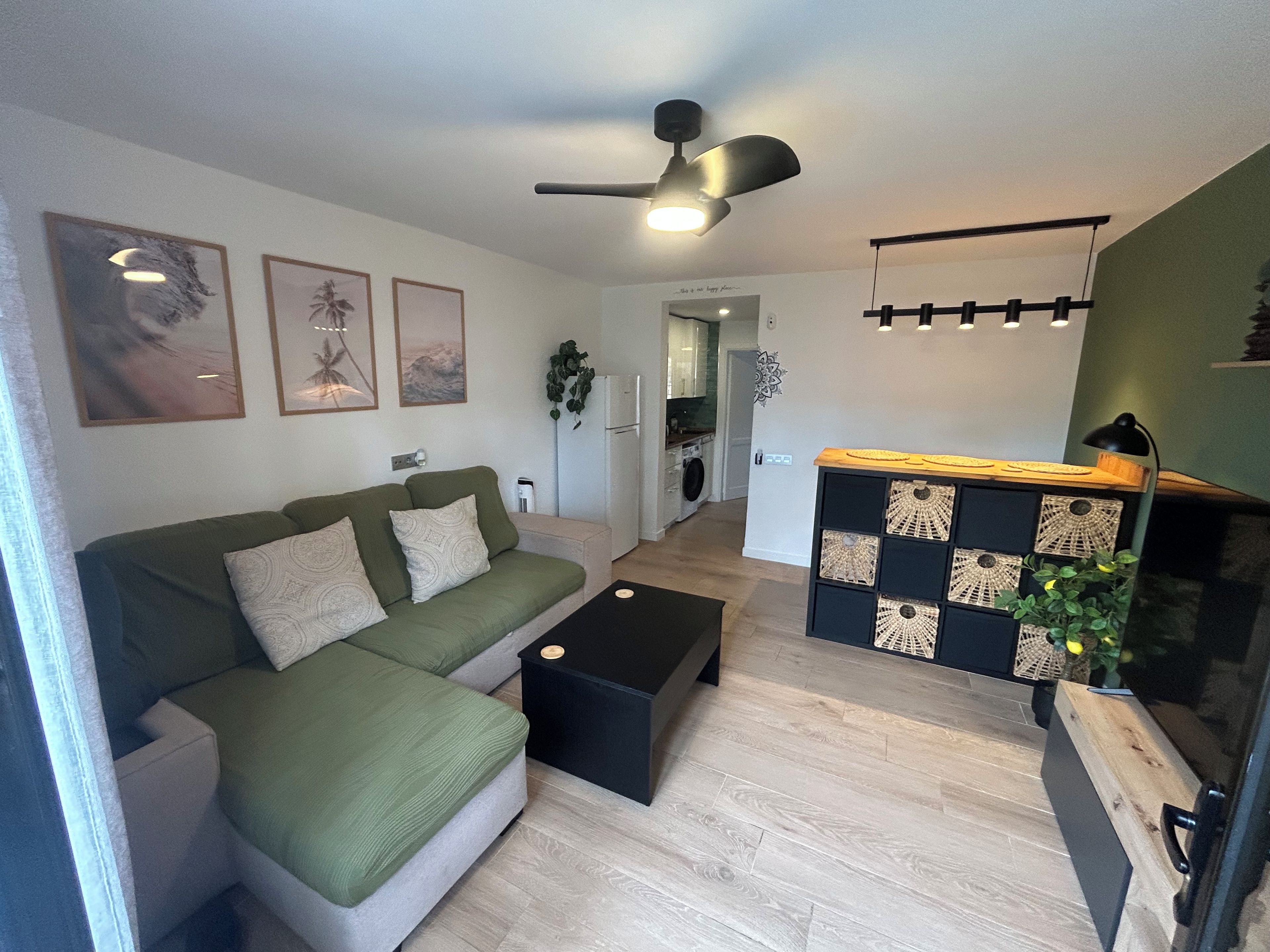A modern living room with a sofa, a coffee table, a ceiling fan, and a kitchen area in the background.