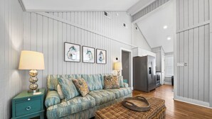 A living room with a sofa, two side tables, a wicker ottoman, and a refrigerator.
