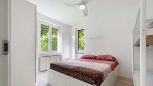 Ett sovrum med en säng, en takfläkt, två fönster och ett element.