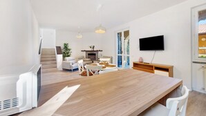 Ett modernt vardagsrum med ett matbord i trä, vita soffor och en tv som är monterad på väggen.