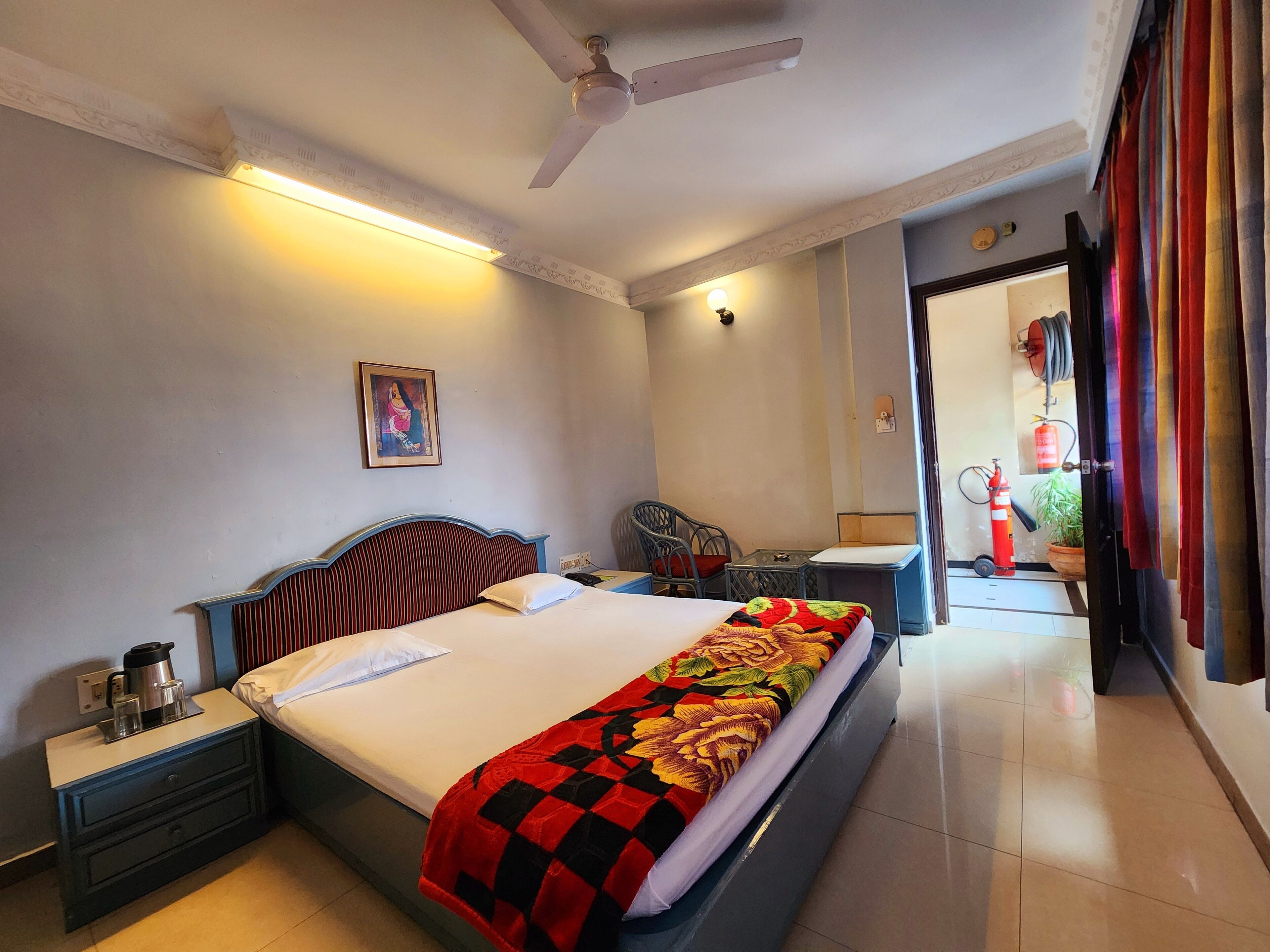 A hotel room with a bed, bedside table, nightstand, ceiling fan, and a small table with a chair.
