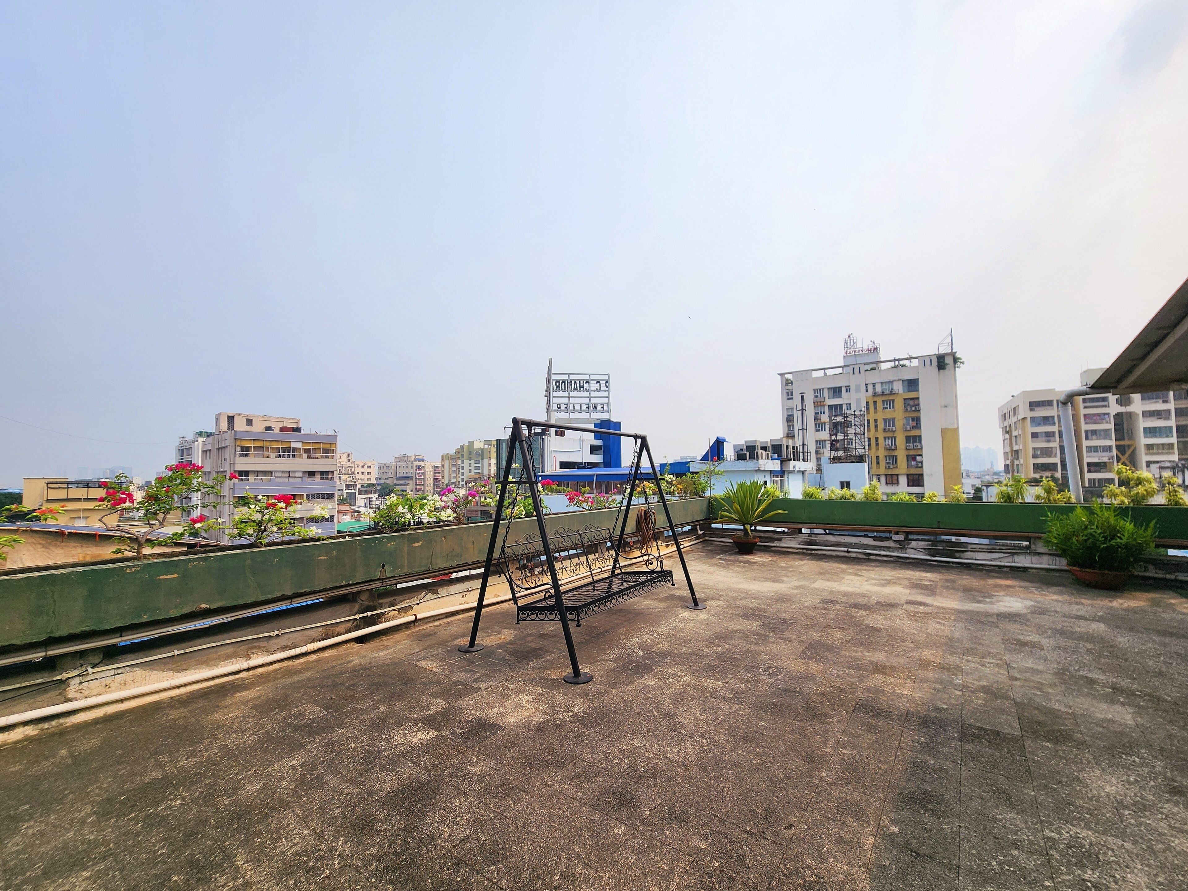 Una terraza en la azotea con un columpio, plantas en macetas y vistas de edificios de la ciudad.