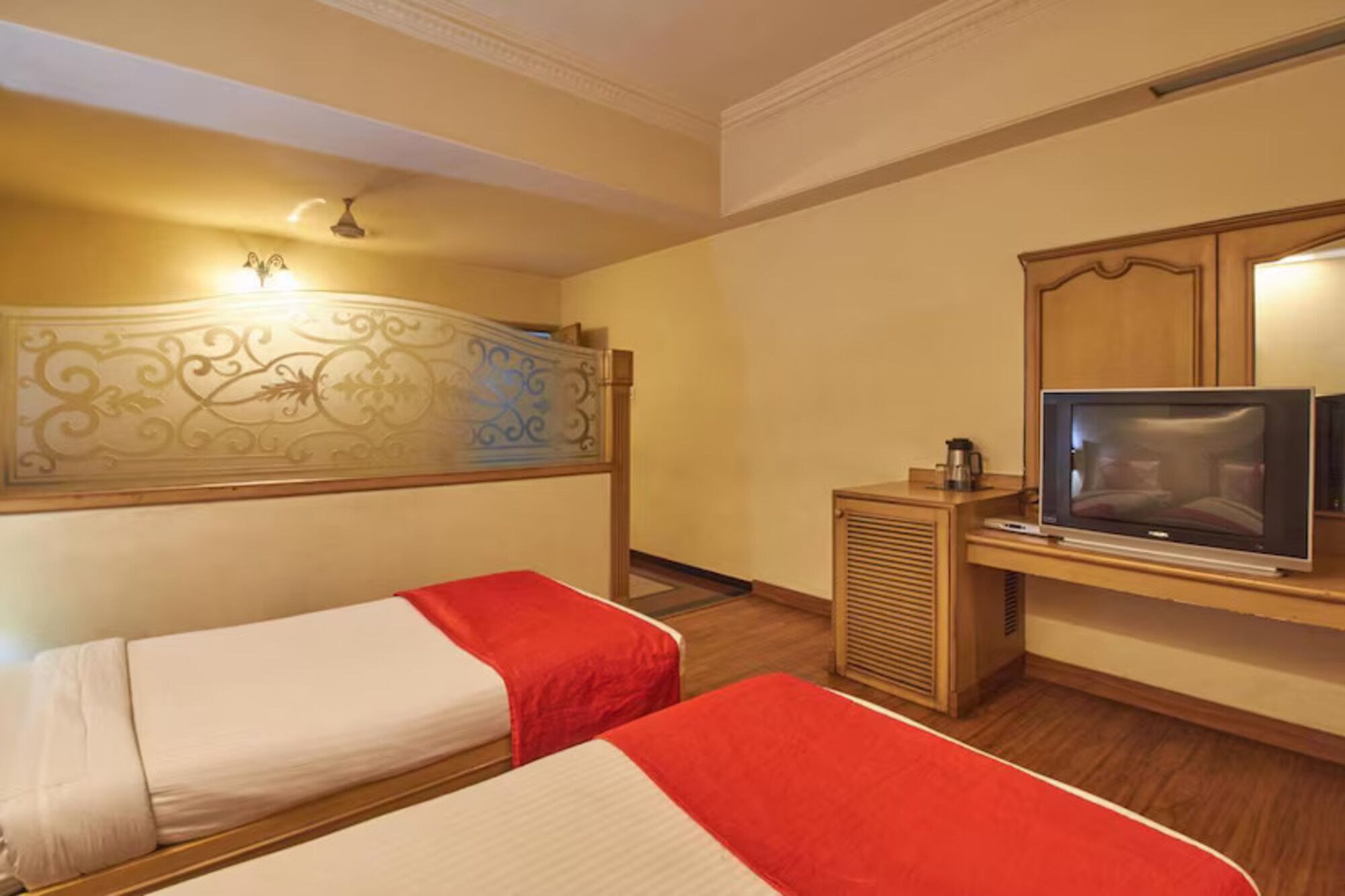 A hotel room with two beds, a television, a heater, and a decorative wall panel.