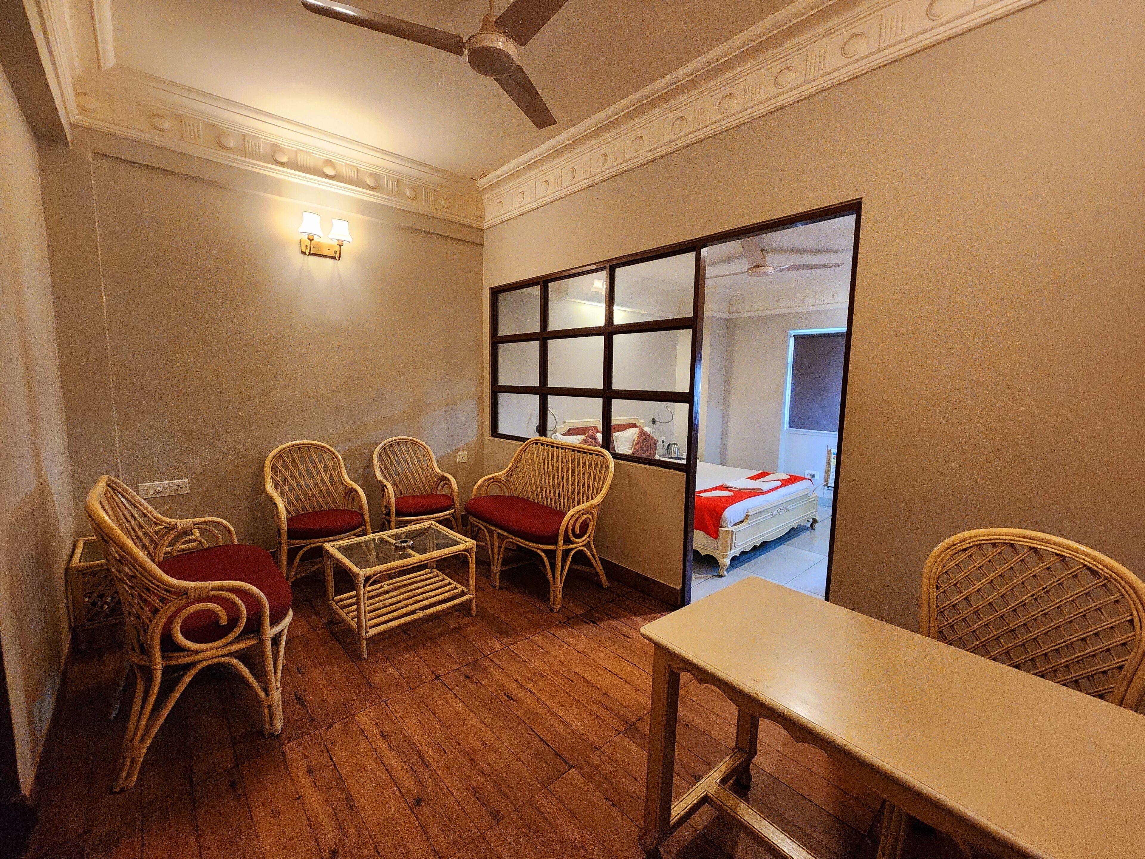 A room with wicker furniture, a glass table, and a bed with a red blanket.