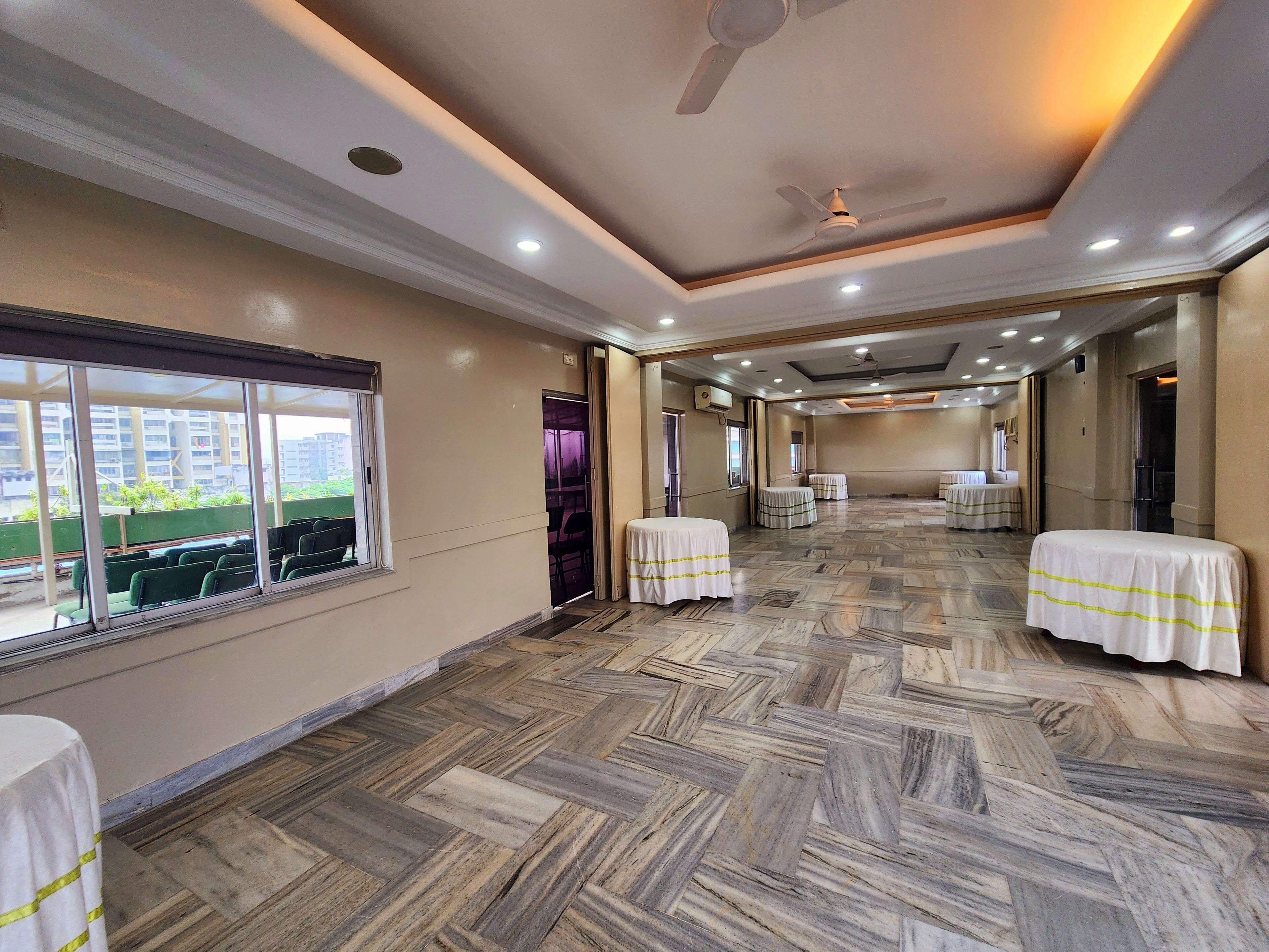A hotel room with a large window, a ceiling fan, and a herringbone-patterned floor.