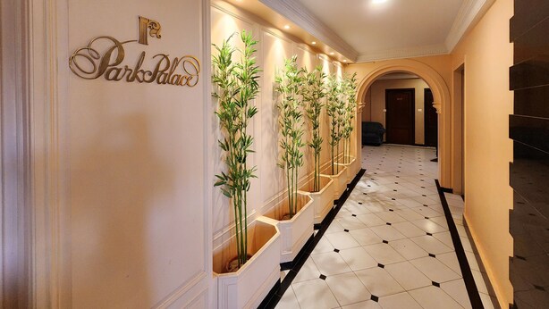 A hotel hallway with a sign reading "Park Palace," a tiled floor, and a row of tall plants.