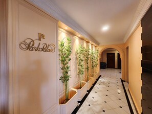 A hotel hallway with a sign reading "Park Palace," a tiled floor, and a row of tall plants.