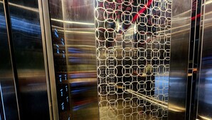 An elevator interior with a metallic door and a patterned glass panel.