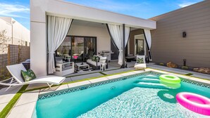 A modern outdoor pool area with a covered patio, lounge chairs, and inflatable rings. - Casa De Amore (Palm Springs)