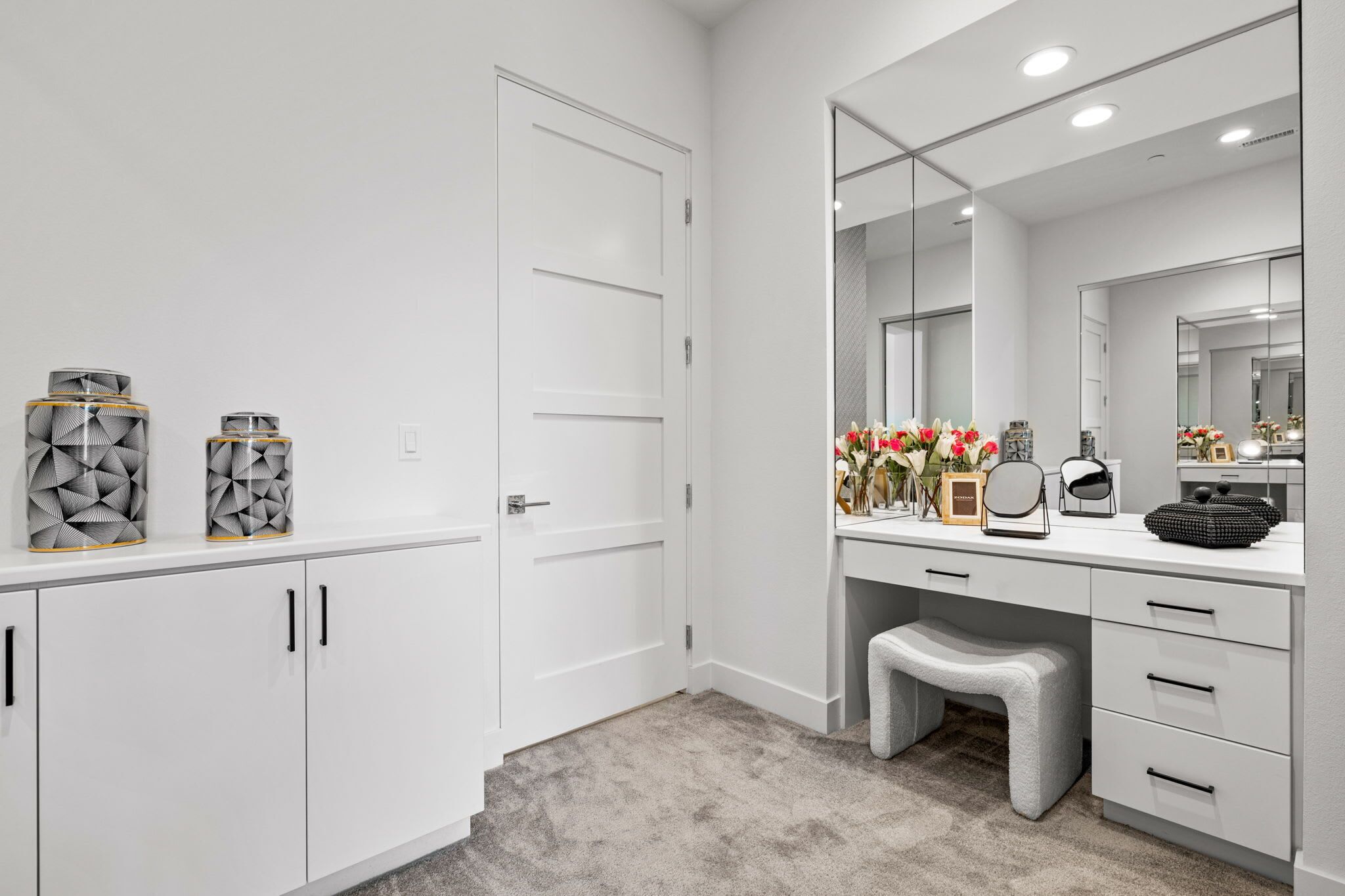 A modern bathroom with white cabinetry, a vanity with a large mirror, and decorative items on the counter.