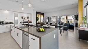 A modern kitchen with a central island, stainless steel appliances, and pendant lighting. - Casa De Amore (Palm Springs)