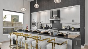A modern kitchen with a central island, stainless steel appliances, and pendant lighting. - Casa De Amore (Palm Springs)