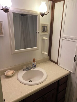 Une salle de bain avec un lavabo blanc, un miroir, un rideau de douche et un distributeur de savon.
