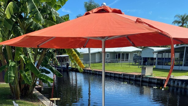 A waterfront patio with white Adirondack chairs, a red umbrella, and a concrete dock extending into a calm body of water. - Lake Okeechobee Hideout - On the water (Moore Haven)