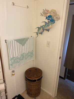 Une salle de bain avec une serviette à rayures, une poubelle en osier et des décorations murales représentant des poissons.