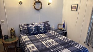 A bedroom with a plaid bedspread, a nightstand with a lamp, a wall-mounted light fixture, and a framed picture. - Lake Okeechobee Hideout - On the water (Moore Haven)