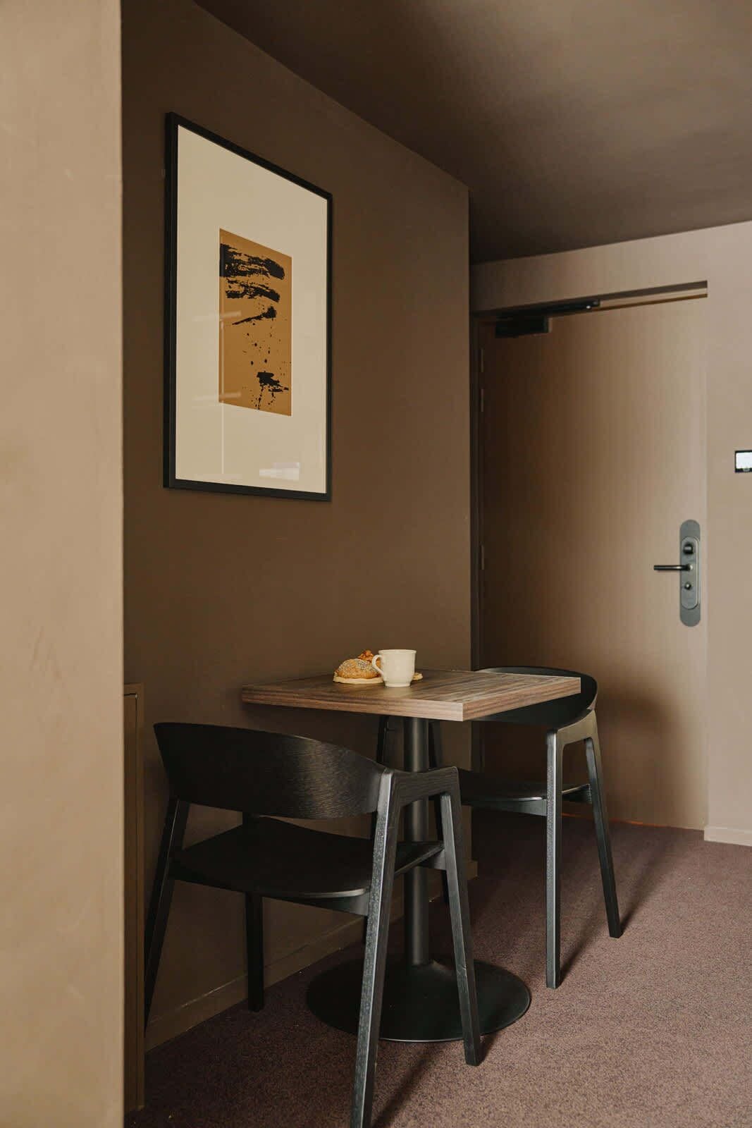 Una habitació petita i acollidora amb una taula, dues cadires, un quadre al mur i una porta amb tirador.