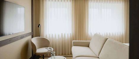 A hotel room with a sofa, armchair, and a flat-screen TV.