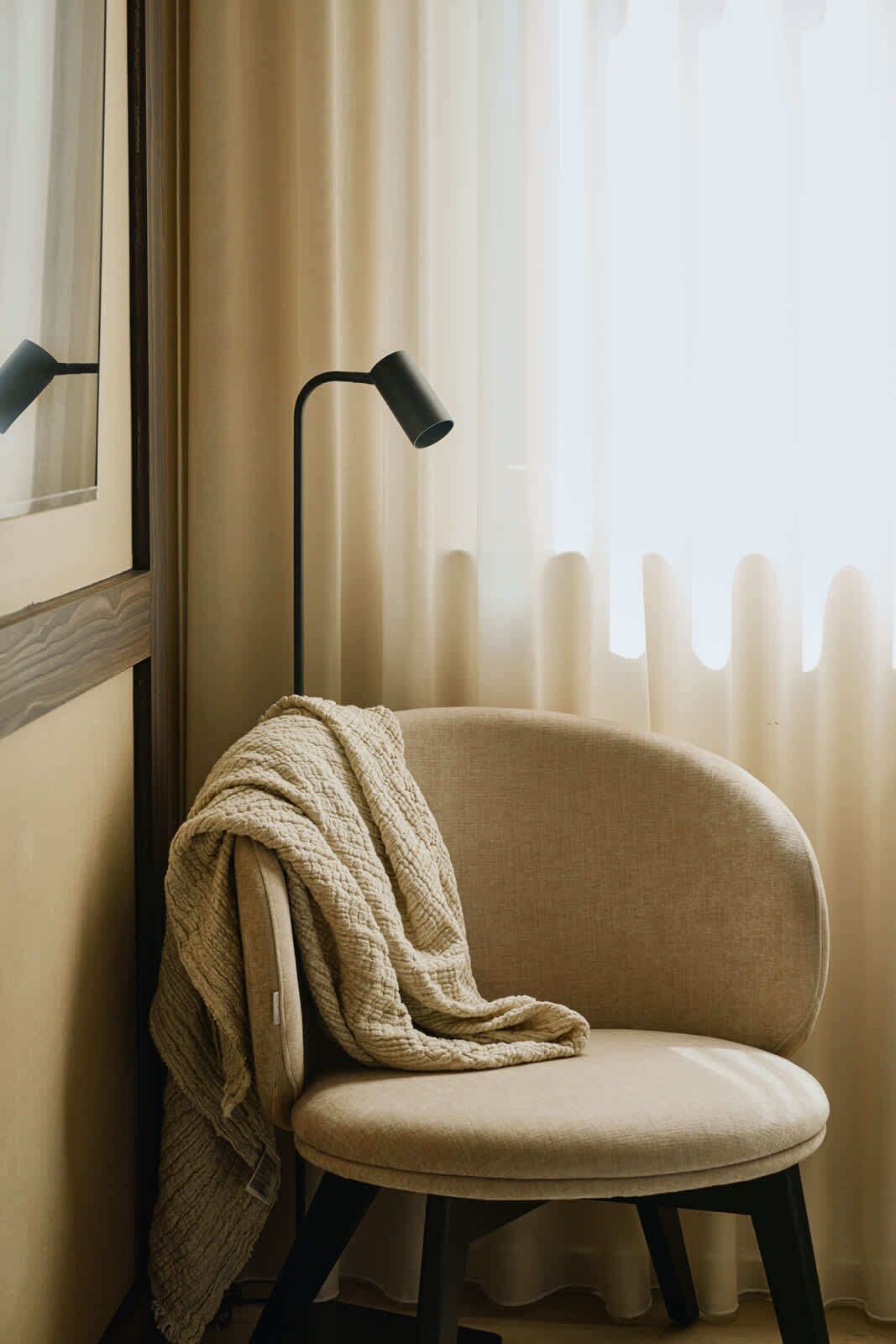 Une chaise avec une couverture, une lampe sur pied et une fenêtre avec des rideaux.