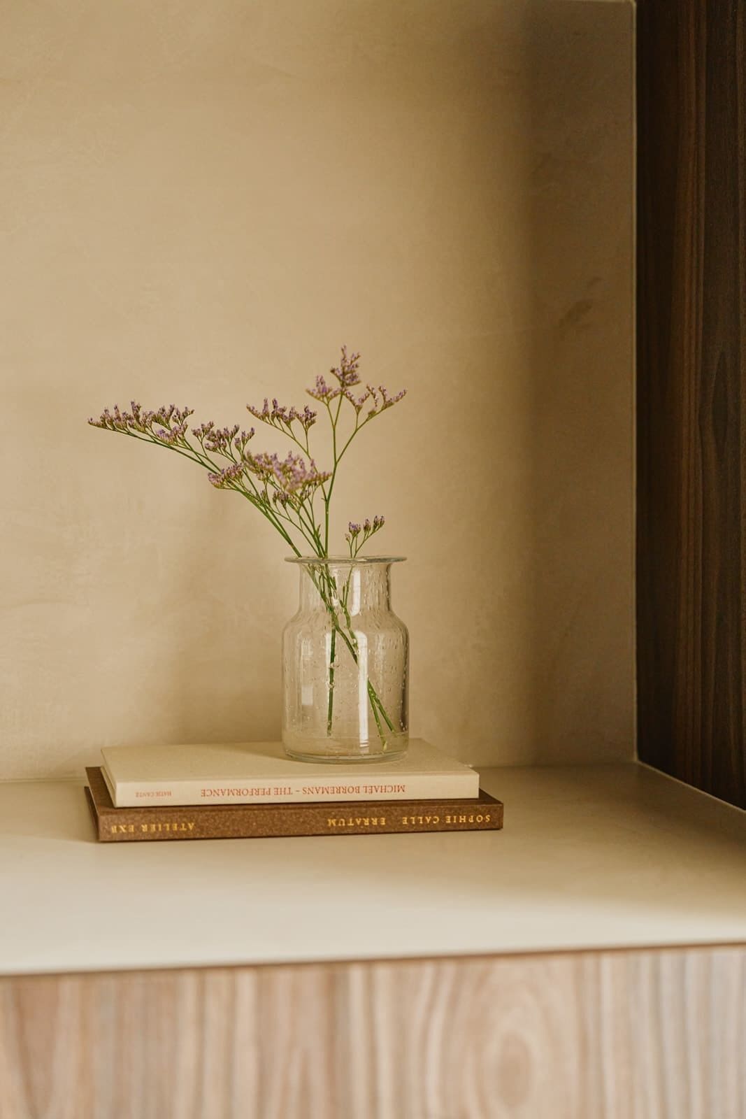 En gennemsigtig glasvase med blomster på en træhylde, bøger nedenunder.