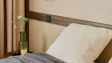 A neatly made bed with a grey striped blanket, a white pillow, and a vase with flowers on a bedside table.