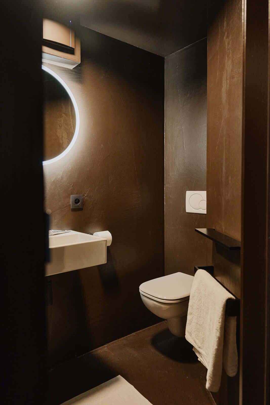 Un baño moderno y compacto con un espejo redondo, inodoro y lavabo.