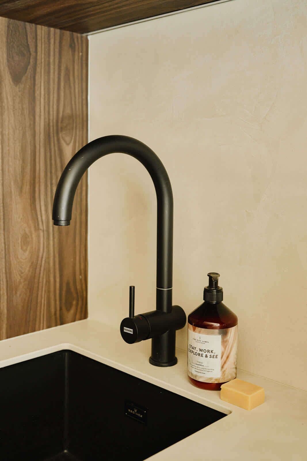 A modern kitchen sink with a black faucet, a soap dispenser, and a bar of soap.