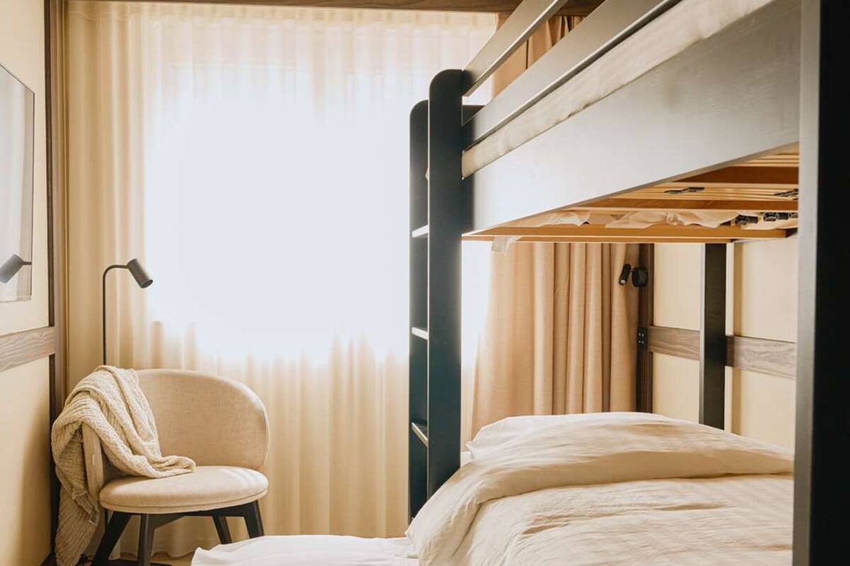 Ein kleines Hotelzimmer mit Etagenbett, einem Sessel und einem Nachttisch.