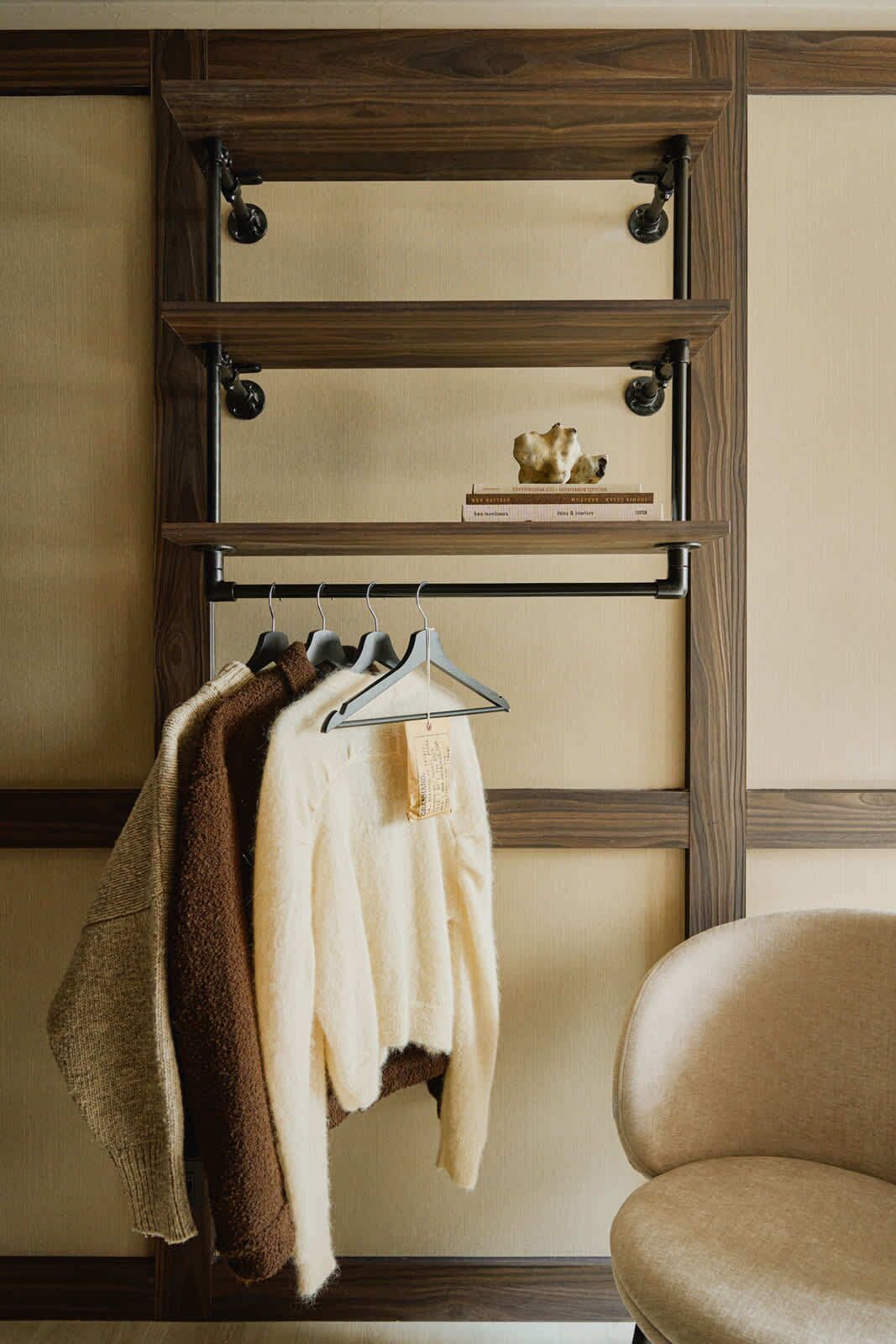 A room with a wooden wall panel, a shelf with a book and a small sculpture, and a chair.