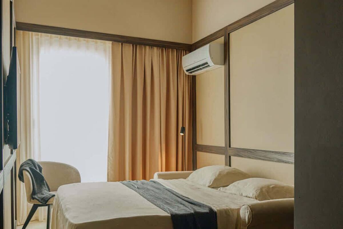 Ein Hotelzimmer mit Bett, Stuhl, Klimaanlage und einem fensterbelaubten Fenster.