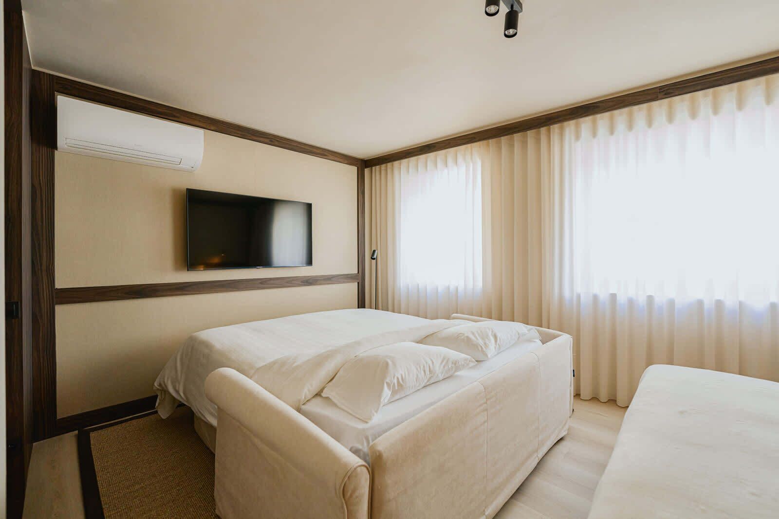 A hotel room with a bed, a television mounted on the wall, and a window with curtains.
