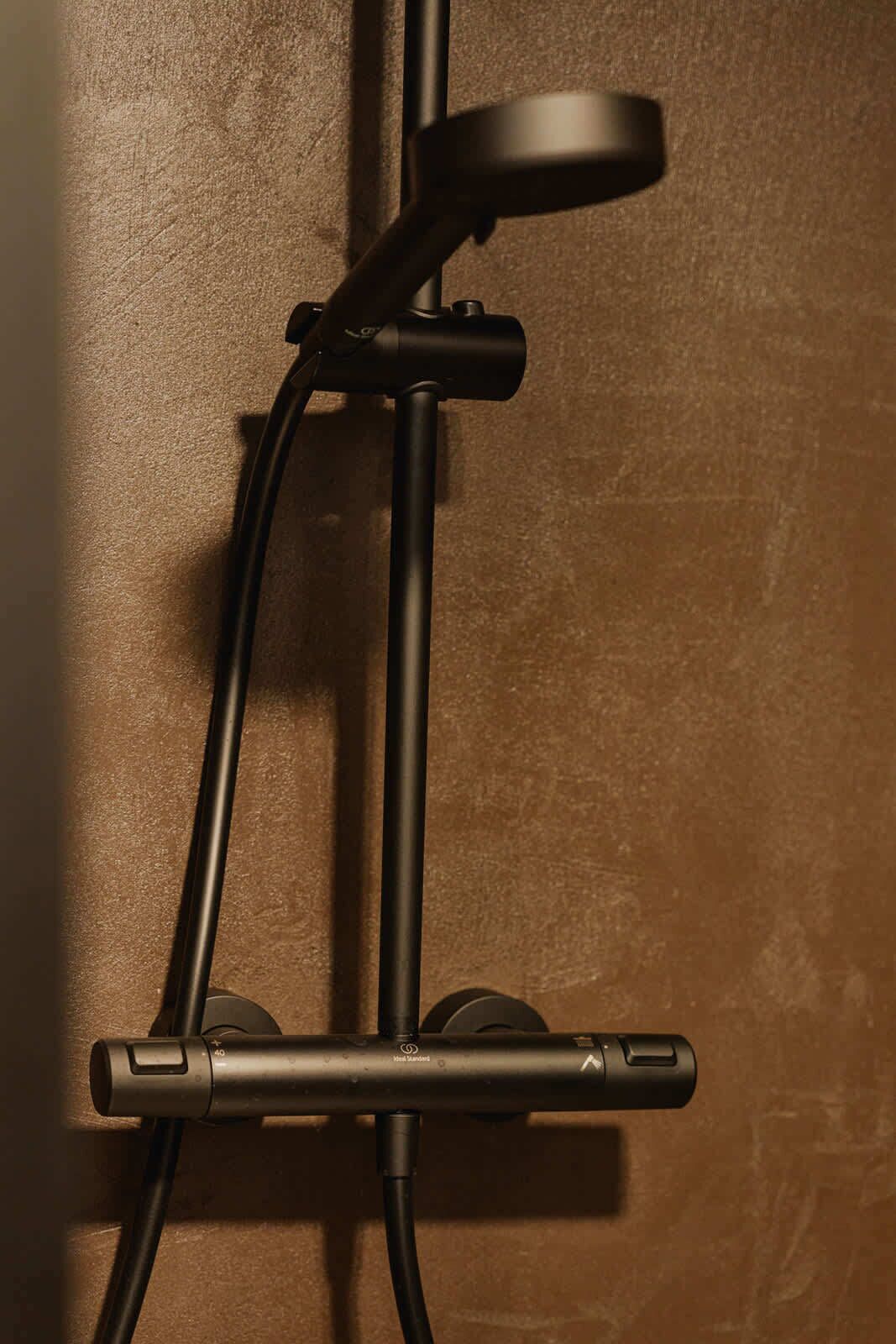 A shower with a handheld attachment and a wall-mounted control panel.