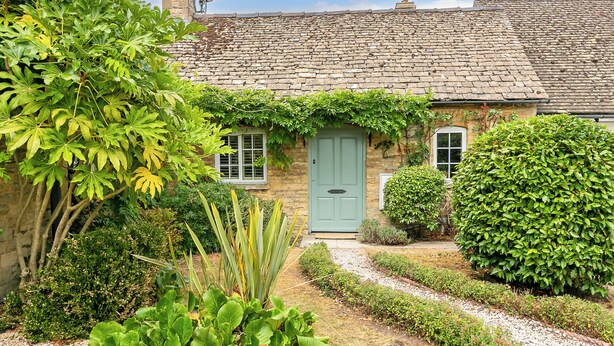 A stone house with a green door, surrounded by lush greenery and a gravel path. - Beautiful 2BD Cottage in the Cotswolds (Churchill)