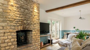 A cozy living room with a stone fireplace, a television, and a comfortable seating area. - Beautiful 2BD Cottage in the Cotswolds (Churchill)