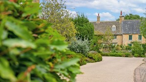 A stone building with a gravel driveway and lush greenery. - Beautiful 2BD Cottage in the Cotswolds (Churchill)