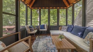 A cozy, enclosed porch with wooden beams, a ceiling fan, and a seating area with a sofa and chairs.
