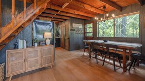 A wooden staircase leading to a dining area with a table and chairs, a cabinet with shelves, and a window with a view of trees.