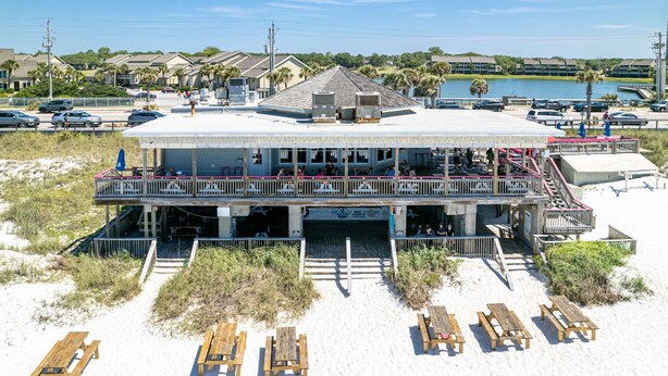 Ein Gebäude direkt am Strand mit Balkon, Außenbestuhlung und Blick auf das Wasser.