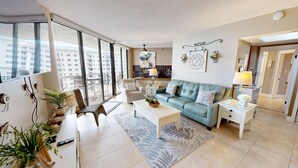 A modern living room with a sofa, coffee table, and chairs, large windows, and a balcony. - Surfside 0708a 2 Bedroom Condo (Miramar Beach)