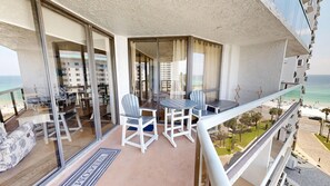 A balcony with a table and chairs, a view of the beach, and a reflection of buildings in the glass door. - Surfside 0708a 2 Bedroom Condo (Miramar Beach)