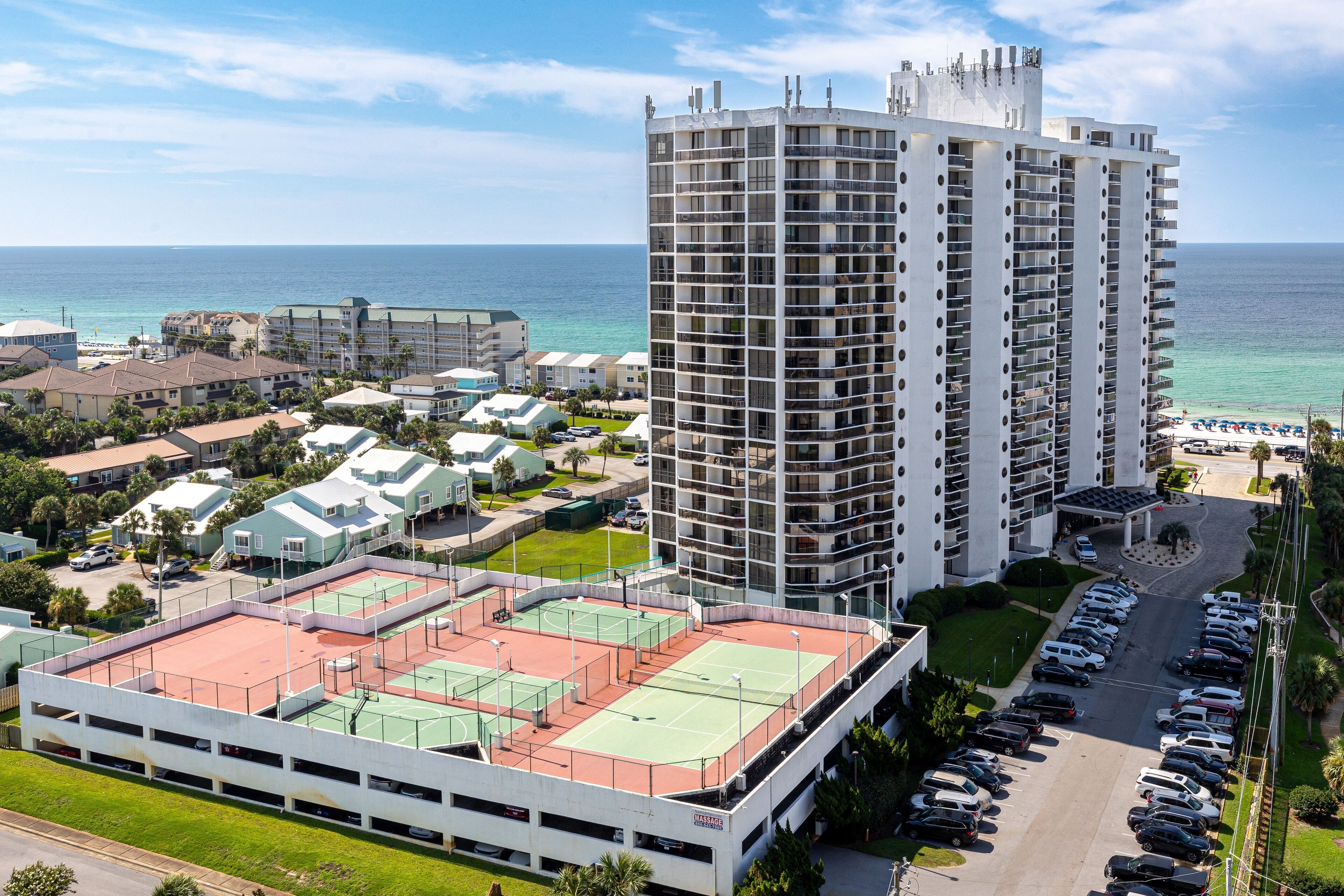 A high-rise hotel with multiple floors, a tennis court, and a parking lot.