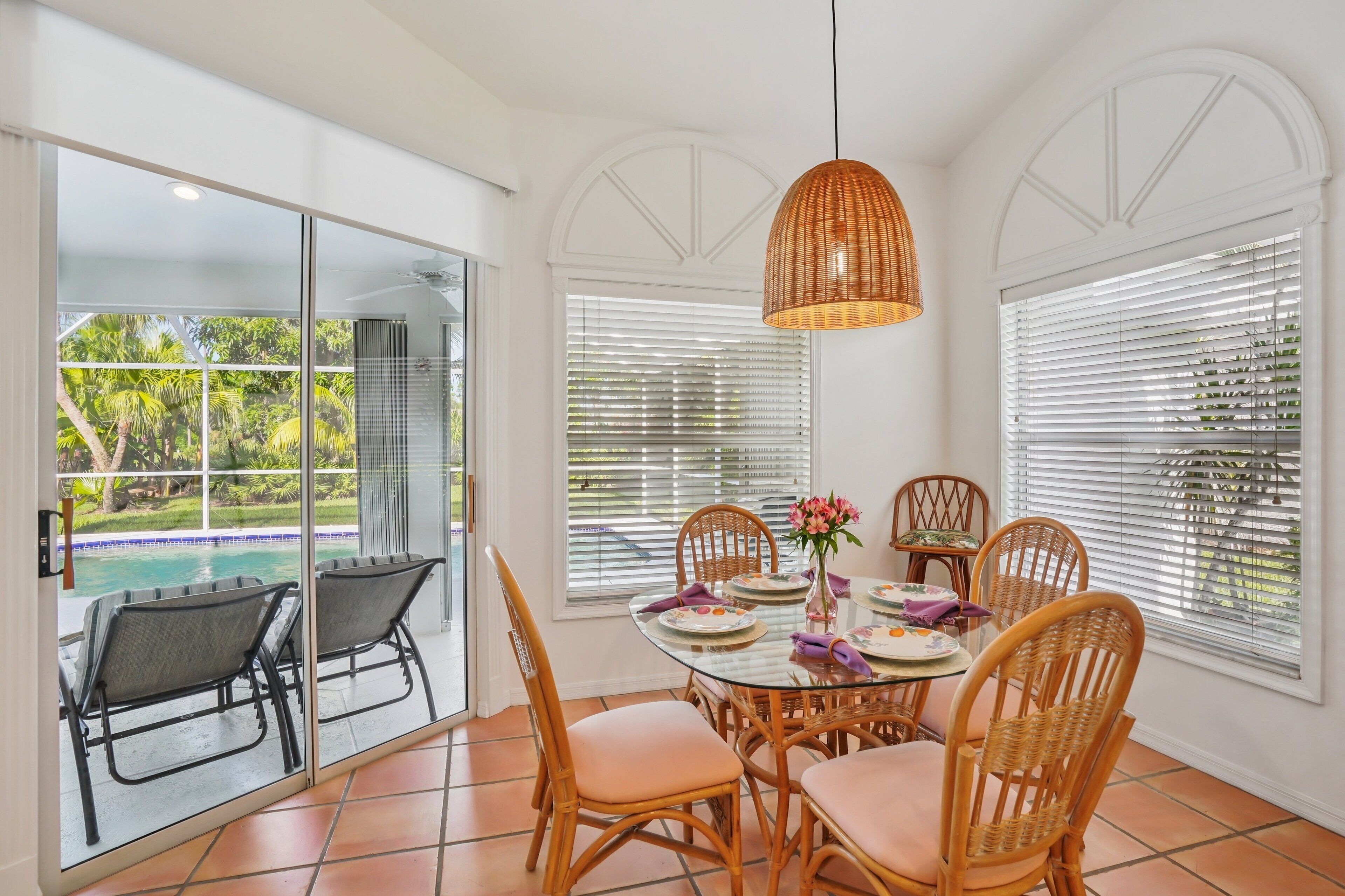 A dining area with a glass table, wicker chairs, and a hanging light fixture.